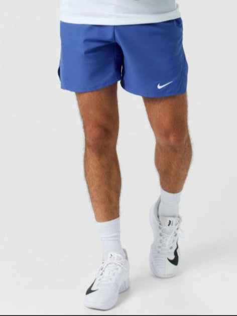 Person wearing blue Nike shorts and white sneakers on a light gray background